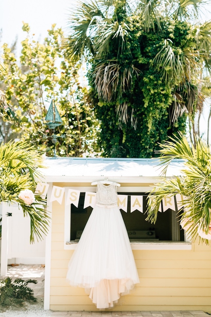 palms and other trees, near a small yellow, wooden beach hut, with a wedding gown hung on the roof, beach weddings in florida 