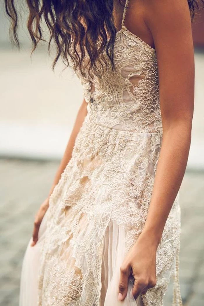 close up of a white and cream-colored, boho lace beach wedding dress, worn by tanned model, with curly brunette hair