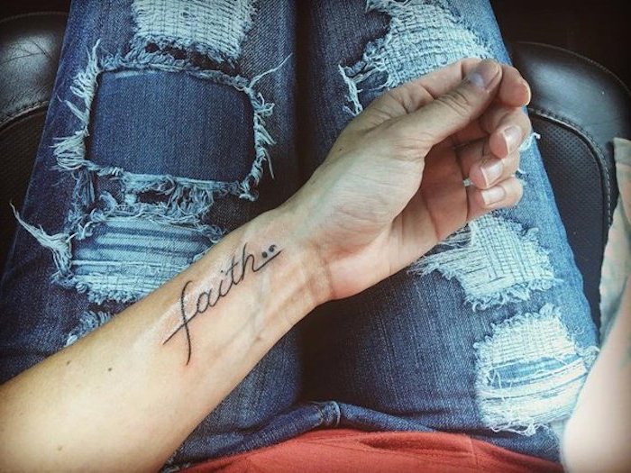 ripped and distressed jeans, and pale coral red top, hand with the word faith tattooed on its wrist, along with a semicolon, suicide awareness tattoo, black flowing font