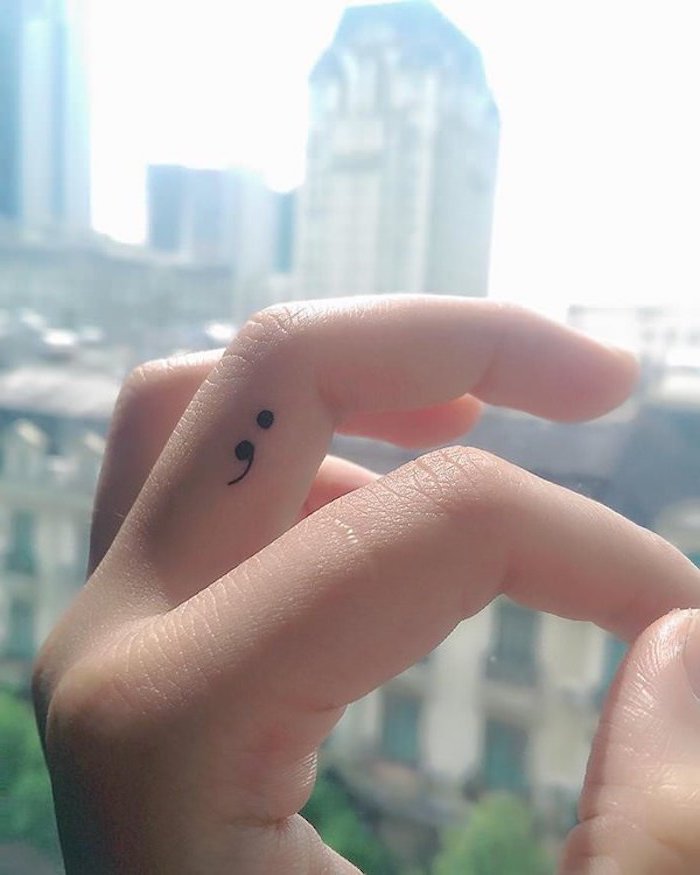 close up of a pale hand, with delicate folded fingers, and small black semicolon tattoo, on the side of the middle finger, semicolon project ideas