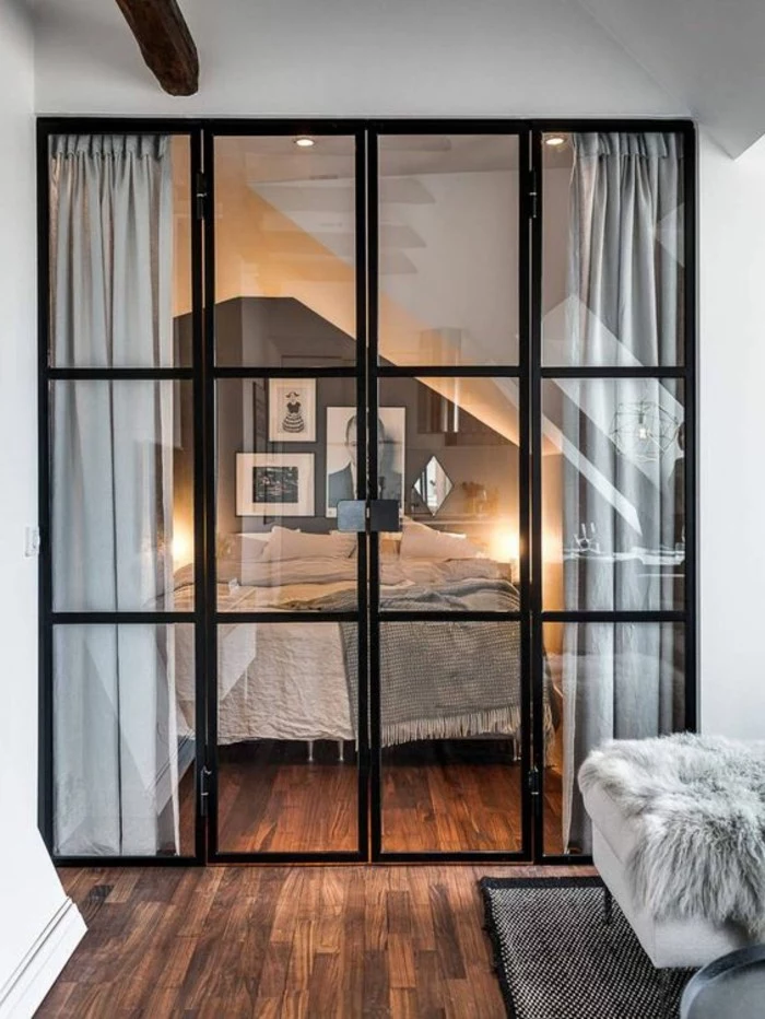 bedroom with dark gray and white walls, and bed with pale gray bed covers, separated from the rest of the studio with folding doors, studio apartment design, brown laminate floor