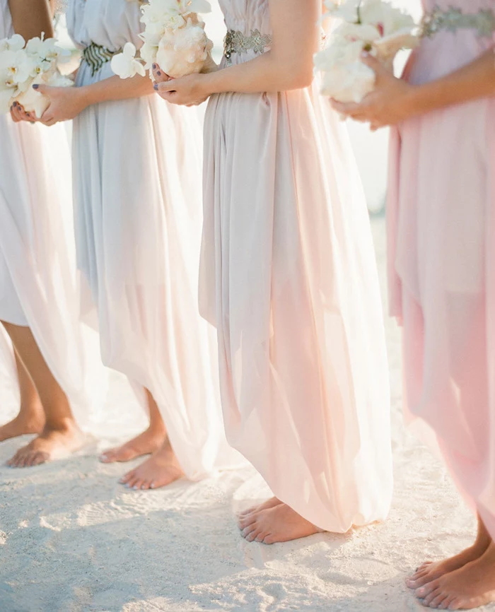 barefoot bridesmaids in pale pink, floaty asymmetrical gowns, with silver belts, each holding a large white conch shell, containing white orchids