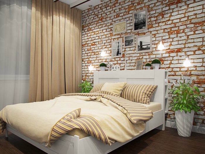 shabby orange and white brick wall, decorated with several framed images, near white bed with pale yellow bedding, wall decor ideas, hanging lights and two potted plants