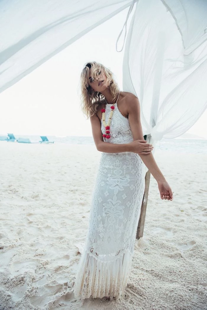 beach with fine white sand, woman with short wet blonde hair, wearing white embroidered halter neck gown, lace details and chunky fabric necklace, beach wedding dresses