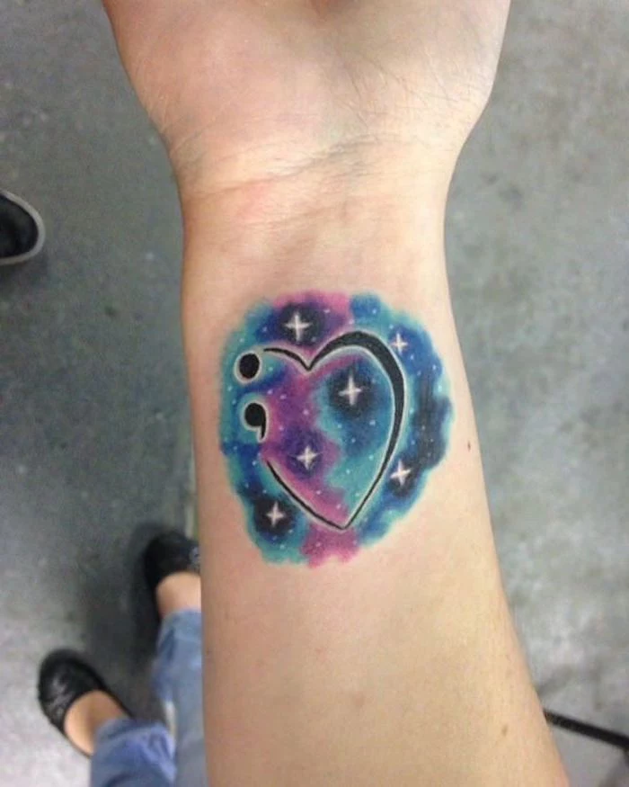 galaxy tattoo in blue, navy and purple, with white stars, and a heart shape in black, decorated with a semicolon, what does a semicolon tattoo mean, beautiful wrist tattoo
