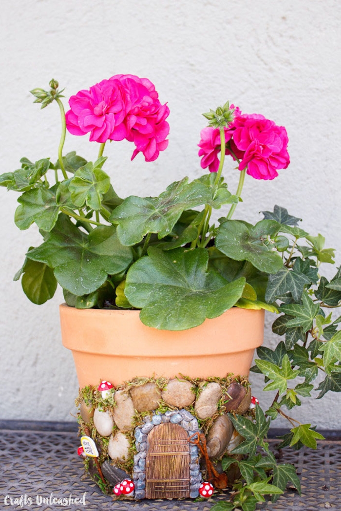 completed decorated planting pot, orange with pebbles, a tiny door and moss, little mushroom ornaments, fairy garden ideas, hot pink flower planted inside