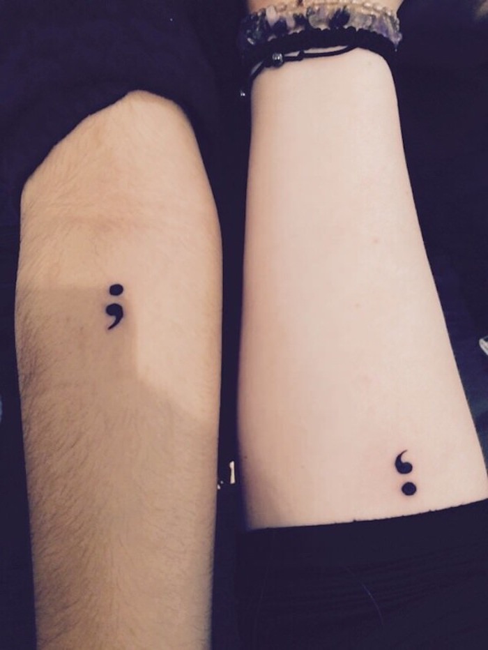 matching semicolon project tattoos in black, on two arms with black sleeves, placed next to each other, one arm is tanned and the other is pale, with several bracelets