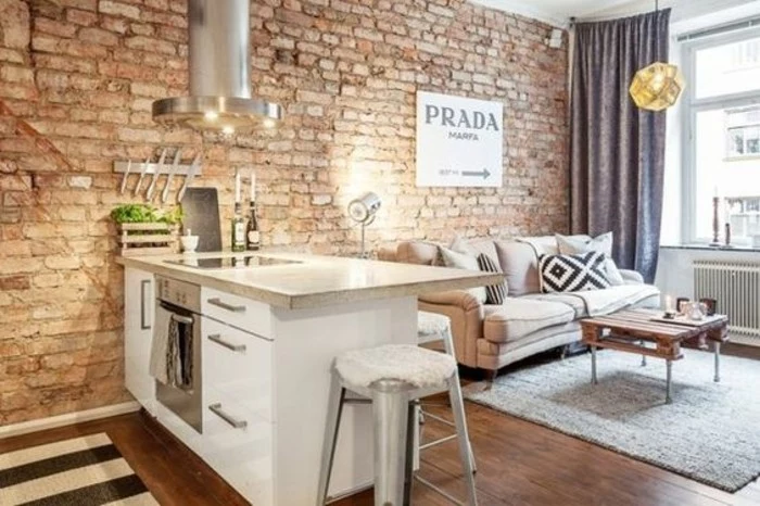 brick wall with industrial feel, inside room with small kitchenette, studio apartment design, off-white sofa and rustic coffee table