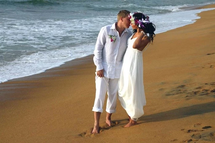 kissing couple dressed in white, floaty grecian gown on a brunette bride, with flowers in her hair, shirt and rolled-up pants on a blonde groom, casual beach wedding dresses