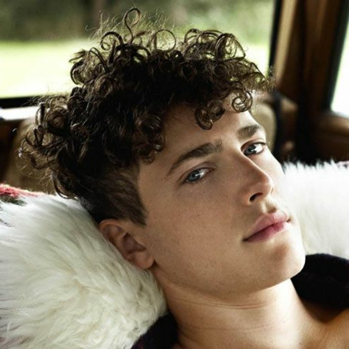 curly haircuts, relaxed young man, leaning on a white fur cushion, wearing a curly quiff, messy on top, short at the sides
