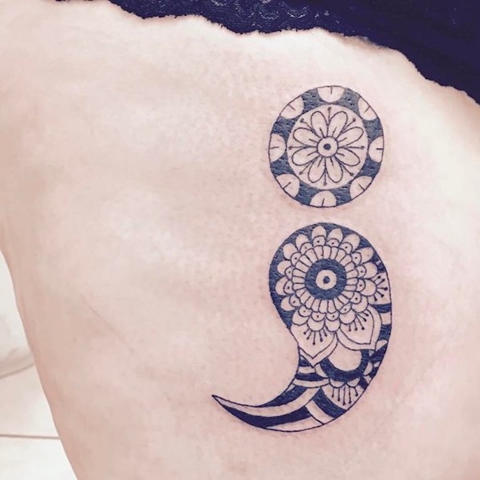 paisley shapes and flower mandalas, in black ink, decorating a large semicolon tattoo, semicolon meaning and significance, on a pale person's back or side