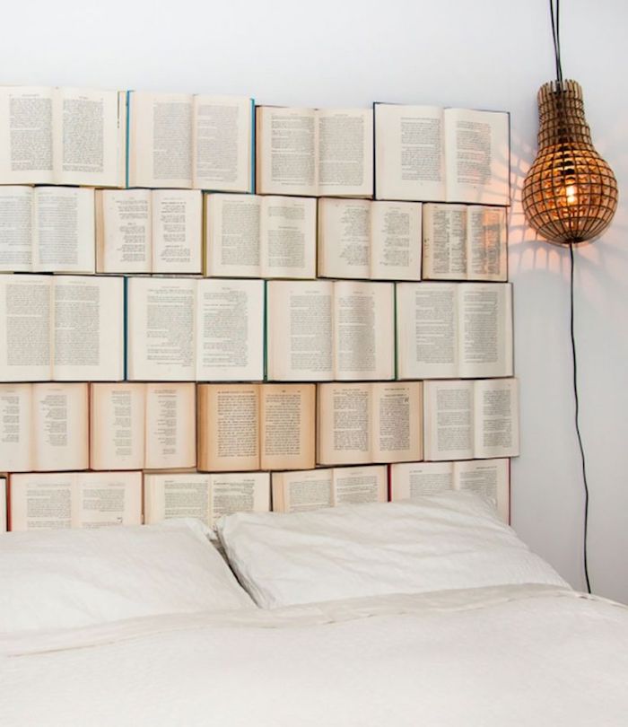 five rows of open books, with white and yellow pages, decorating a white wall, behind a double bed, and near a unique hanging lamp, wall decor ideas 