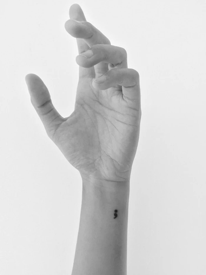 outstretched slim hand, with long slender fingers, and a tiny black semicolon tattoo, on the side of the wrist, black and white image, purpose of semicolon
