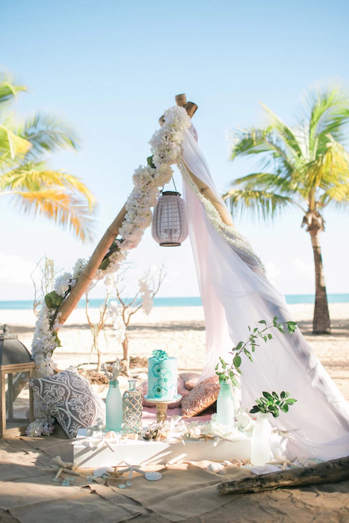 tent in boho style, decorated with flower garlands, lanterns cushions and bottles, on a sandy shore, near the sea, beach wedding venues, palm trees in the background