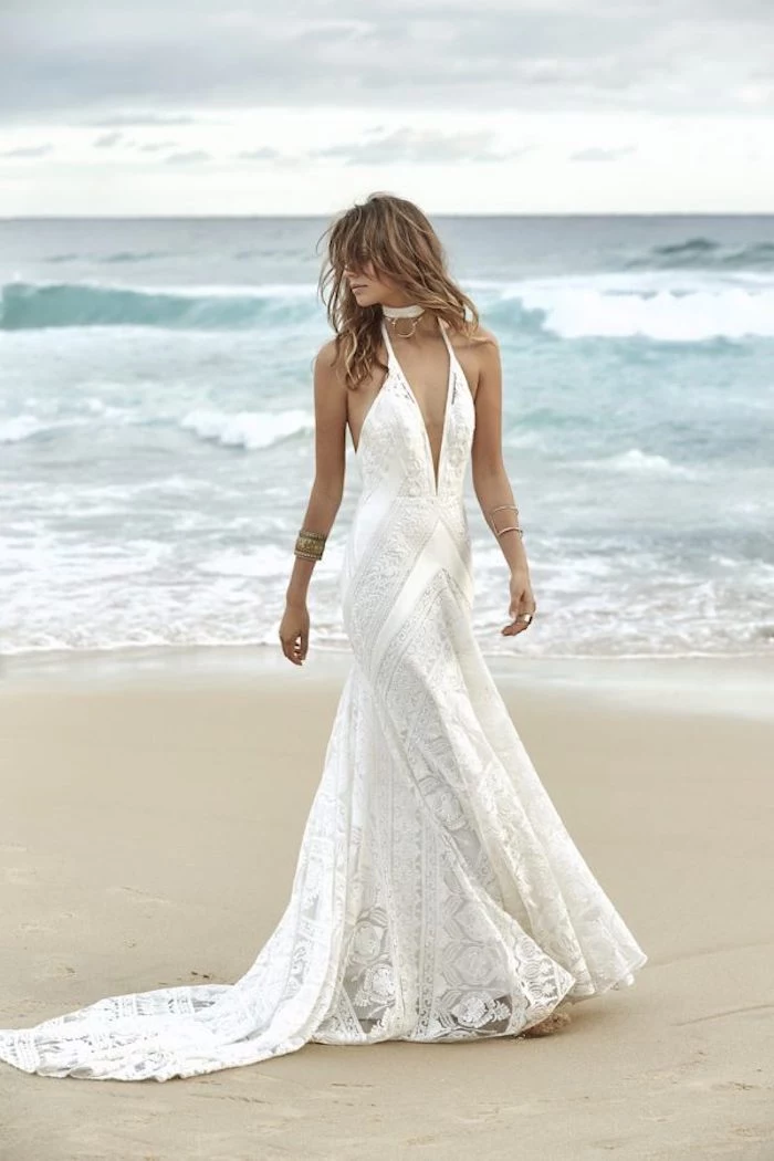 tousled light brunette hair with bangs, on tanned model in white lace beach wedding dress, with plunging neckline, standing on a sandy sea shore