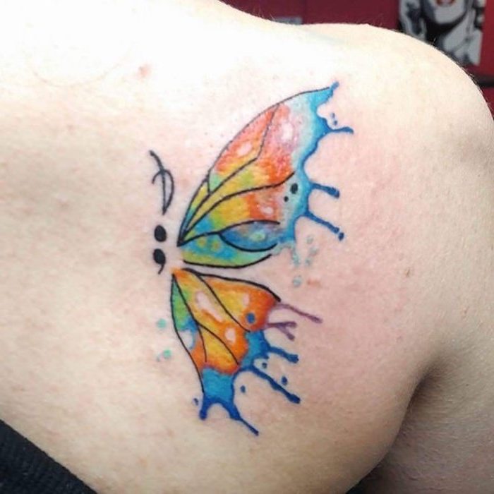 shoulder tattoo of a butterfly, with a semicolon body, and wings with watercolor effect, in blue and purple, green and yellow, orange and red, semicolon movement