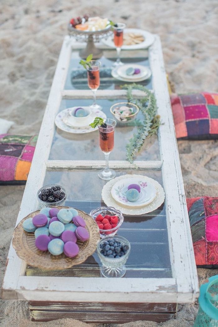 plate of macaroons, dishes with different berries, and glasses containing a pink cocktail, on a rustic outdoor table, made from a used window and two wooden crates