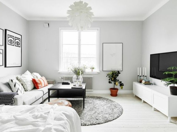 studio apartment decorating ideas, white room with round gray fluffy rug, off-white sofa with several cushions, white cupboard and large TV, lamp and coffee table