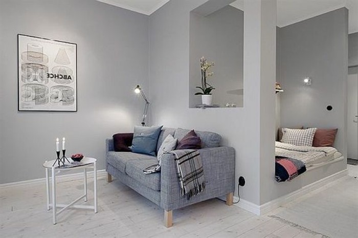 framed poster on gray wall, inside small home, with semi-detached sleeping area, studio apartment design, gray sofa and small coffee table