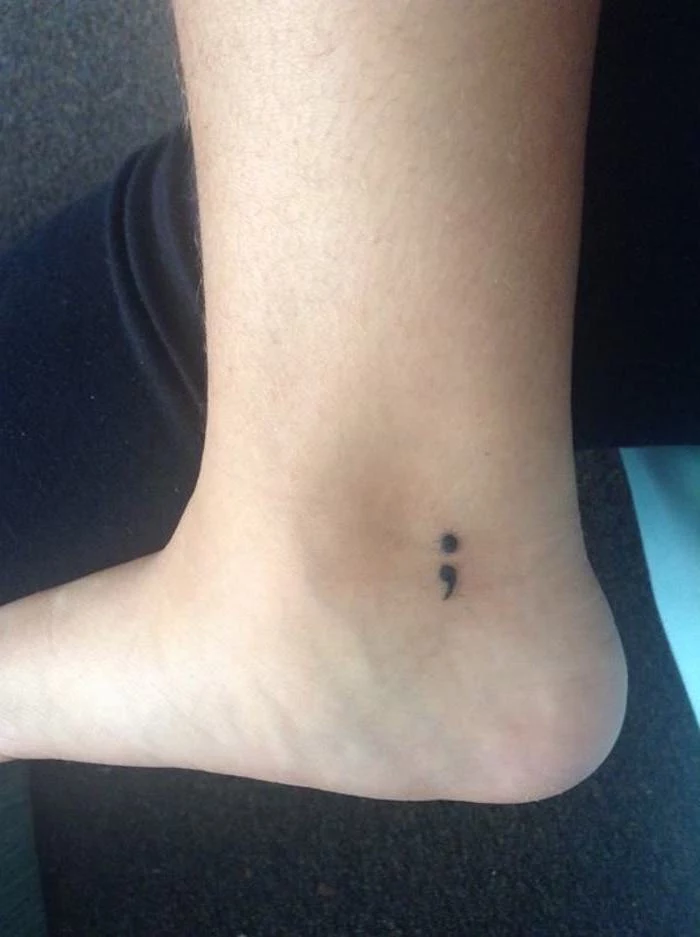 heel tattoo in black, depicting a small semicolon, close to the ankle, inspired by the semicolon movement, simple and minimalistic design