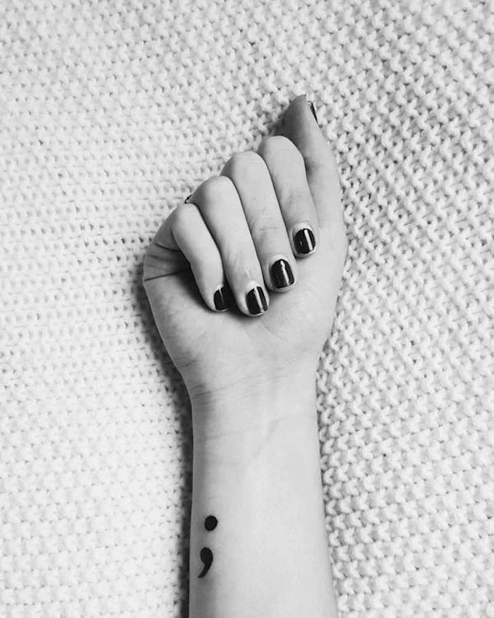nail polish in a dark color, on hand with folded fingers, with small black semicolon tattoo, on the side of the wrist, semicolon movement, black and white photo