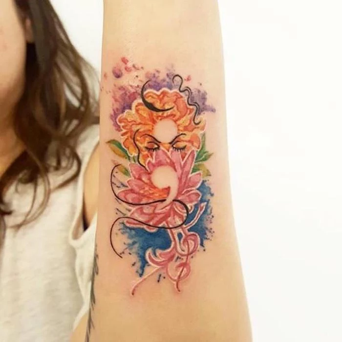 elaborate floral tattoo, in orange and pink, blue and green, purple and black, with subtle semicolon tattoo hidden within, on a woman's arm