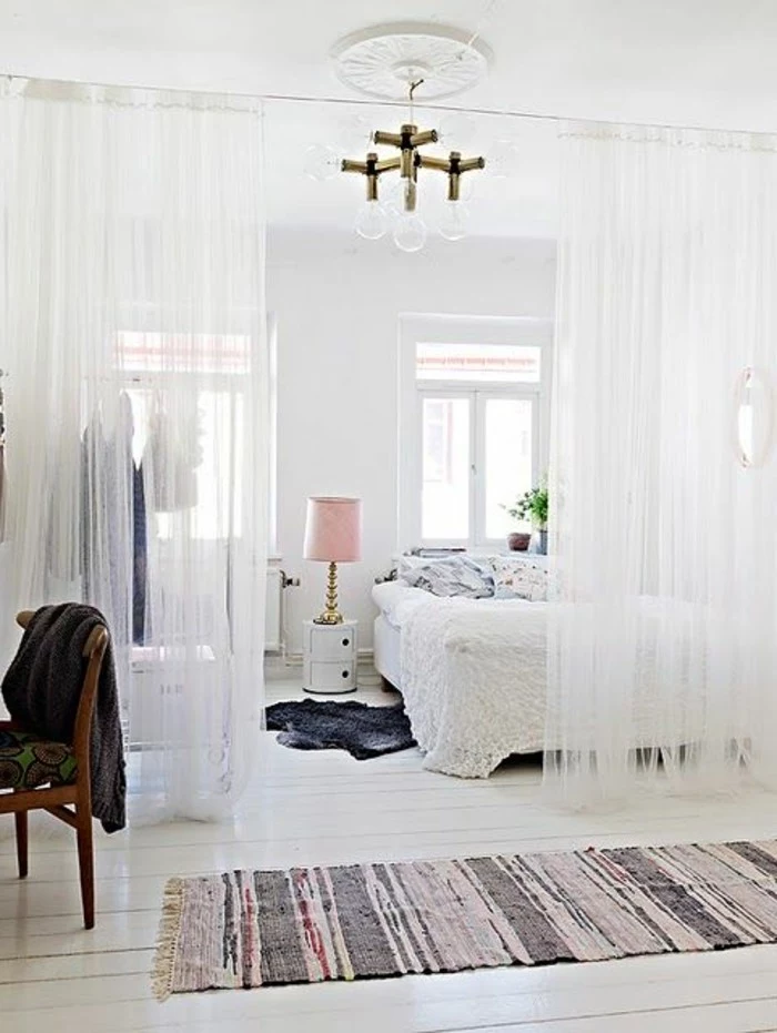 half-drawn curtains, made from sheer-white fabric, separating a sleeping area with white bed, how to decorate a studio apartment, ivory-colored wooden floorboards, vintage chair and rug