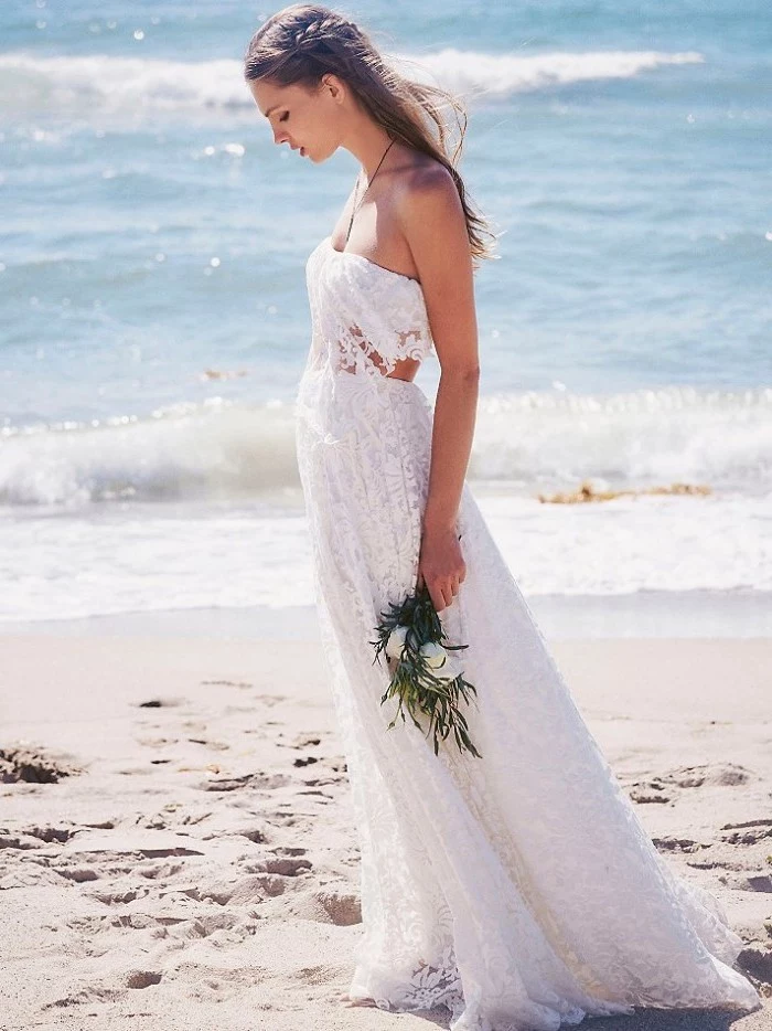 sleeveless white gown, with lace and cutout details, casual beach wedding dresses, worn by young brunette woman, with a single side-braid, holding bouquet of white flowers