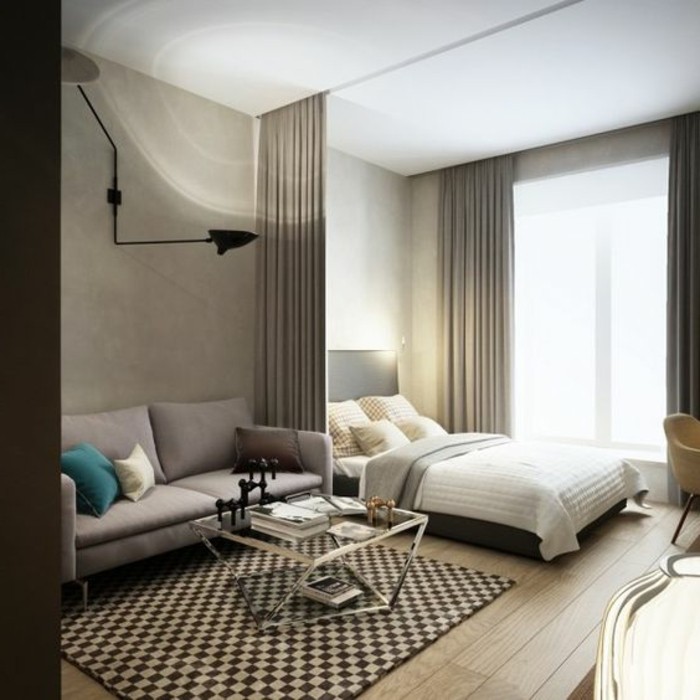 chequered rug in dark brown and cream, on light laminate floor, inside room with gray and white walls, bed with a drawn gray curtain, sofa and coffee table