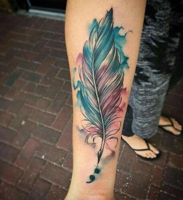 feather quill tattoo with black outlines, and blue and pink watercolor effect, near small black semicolon tattoo, on a woman's hand and wrist