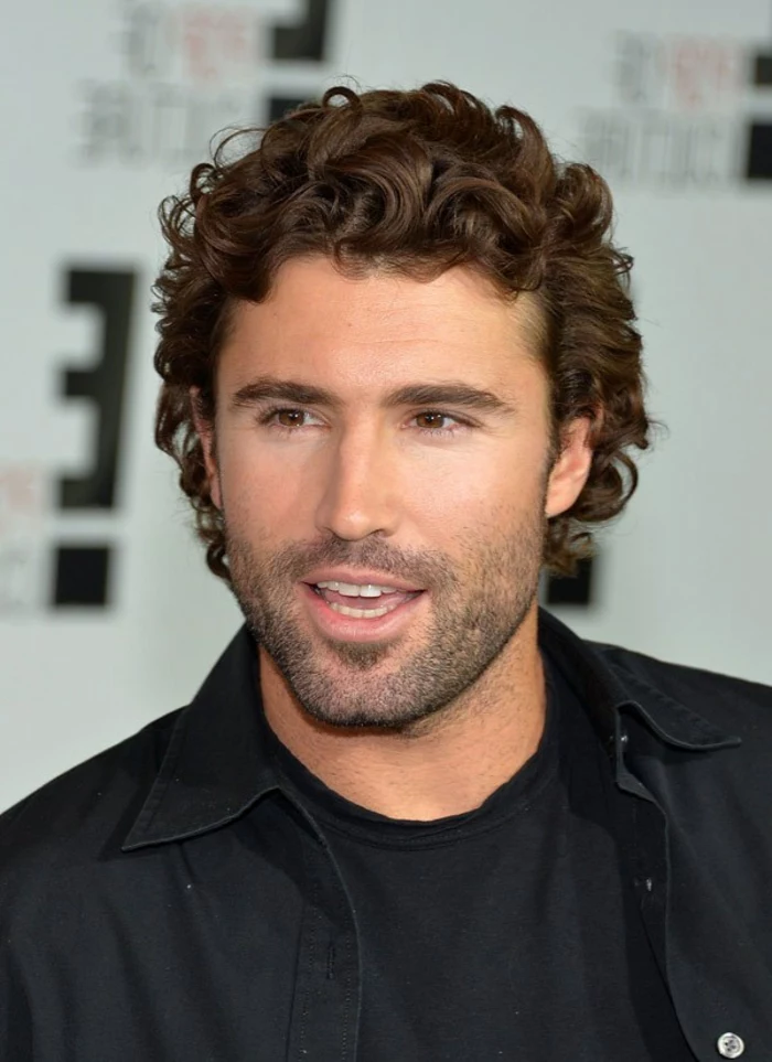 talking man with stubble on his lower face, soft warm brown curls, guys with curly hair, black shirt worn over a black t-shirt