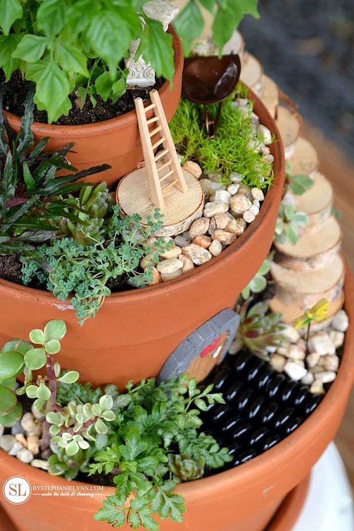 ladder of tiny size, and small door ornament, fairy garden pictures, three orange ceramic pots, stacked on top of each other, and filled with pebbles, dirt and various plants