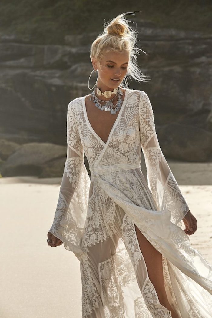 tanned blonde woman, wearing a sheer ivory-colored, embroidered wrap-over lace gown, casual beach wedding dresses, chunky metal jewelry and a messy top knot 