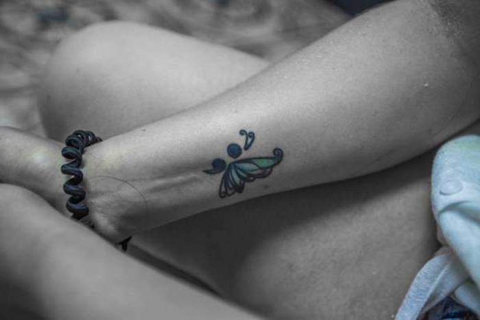 contrasting tattoo of a butterfly, with blue semicolon body, and turquoise wings, with black outlines, on a grayscale image, with small splashes of color
