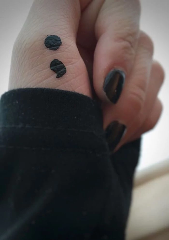 hand-painted temporary tattoo, done with black marker, on a person's thumb, fingers with black nail polish, black jumper sleeve