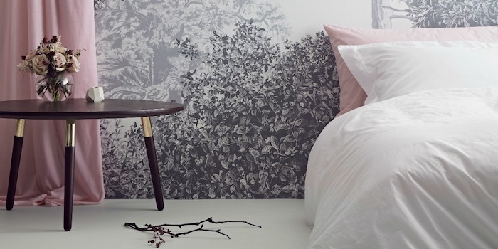 rose bouquet inside a small clear vase, on dark three-legged bedside table, pink curtains near white wall, with pale gray mural