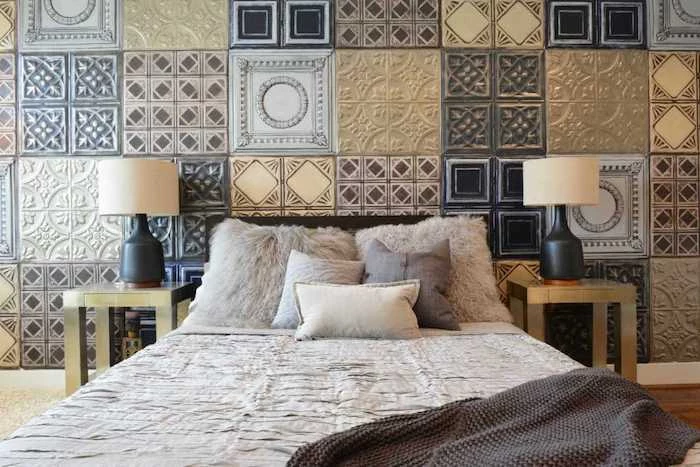 various square tiles, with different patterns and colors, covering the wall behind a double bed, two identical nightstands and lamps