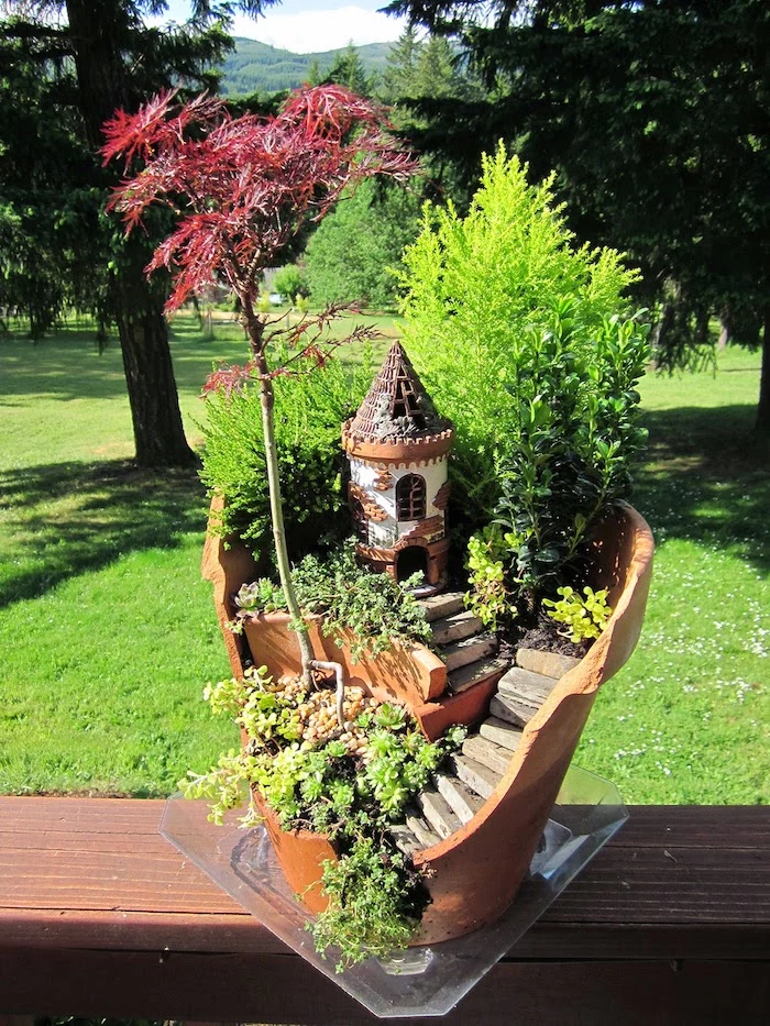 castle fairy tower, made from painted plaster or clay, inside a broken ceramic pot, with little stairs, bonsai tree and shrub, various tiny green plants
