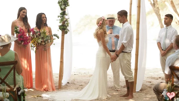 casual nuptials ceremony, an example of beach weddings in florida, two bridesmaids in peach colored maxi dresses, holding large bouquets, blonde bride in white gown, barefoot groom in light relaxed clothing
