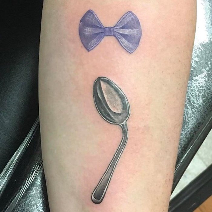 bow in violet and white, and bent silver spoon, positioned so as to form a semicolon, symbolic semicolon meaning, tattooed on the inside of a person's arm