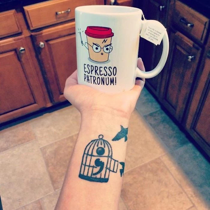 birdcage with open door, containing a semicolon, tattooed on a person's arm, near two birds in flight, hand holds a white mug, with a comical cartoon and message, semicolon tattoo on wrist 