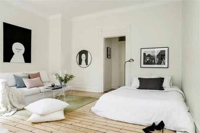 square and round artworks in black and white, inside minimalistic room, how to decorate a studio apartment, pale wooden floor, sofa and bed in white