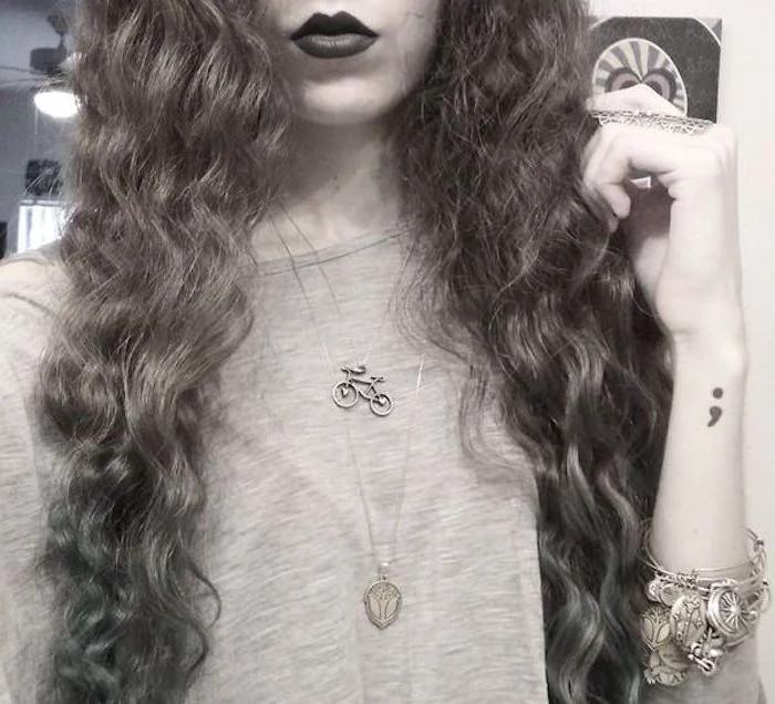 long curly hair, and dark lipstick, worn by woman with lots of jewelry, and a semicolon tattoo on wrist, cropped greyscale photo