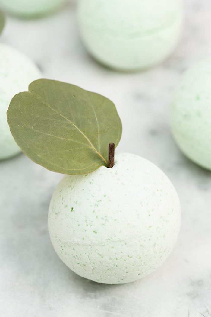 leaf from an apple, and a tiny stem, placed on top of a pale green, spotty bath bomb, bath fizzies made at home