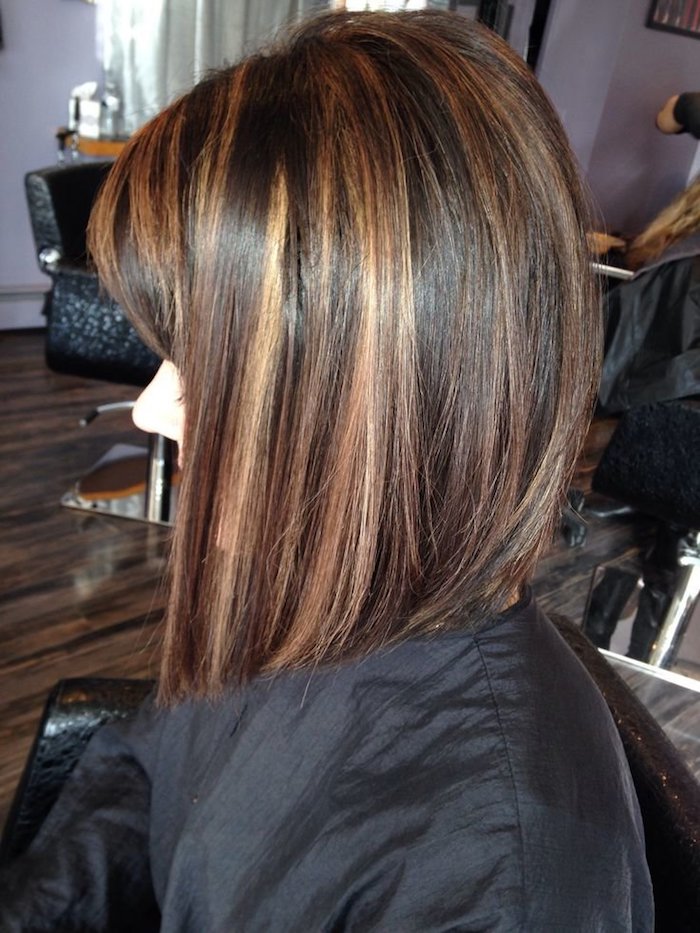 caramel highlights, on dark brunette hair, cut in a asymmetrical bob, and worn by a young woman, sitting in a hairdresser's salon