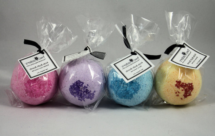 packaged bath bombs, in clear foil, with black ribbons and labels, four in total, in dark pink, light purple and blue, pale yellow with dark brown sprinkles