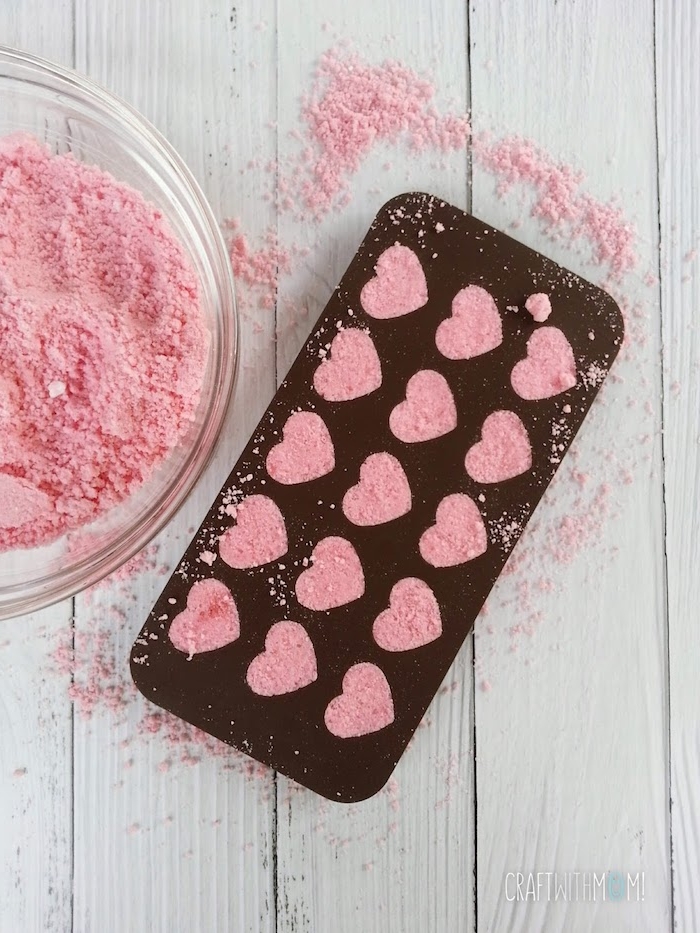 diy bath bombs, brown ice tray, with heart-shaped compartments, filled with coarse pink powder, clear glass bowl with more of the same powder nearby