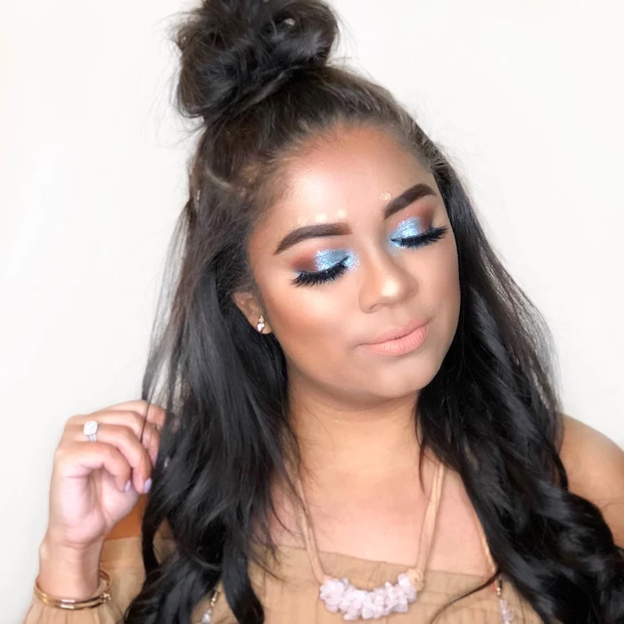 topknot on girl with long dark, partly-curled brunette hair, makeup ideas, blue and brown sparkly eyeshadow, nude pink lipstick