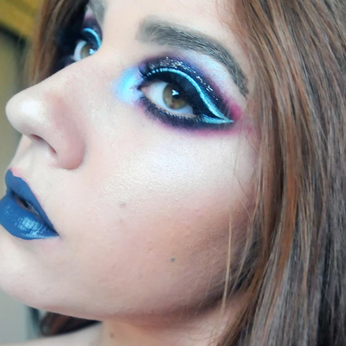 layered eyeshadow in black, pink and different shades of blue, decorated with glitter, worn by woman with blue lipstick