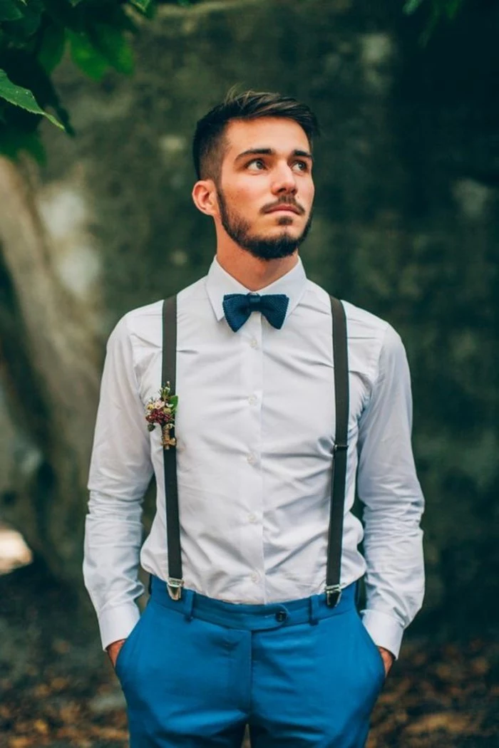 suspenders with a boutonniere, worn with a blue shirt, and teal blue trousers, mens wedding guest attire, on young man with a bowtie